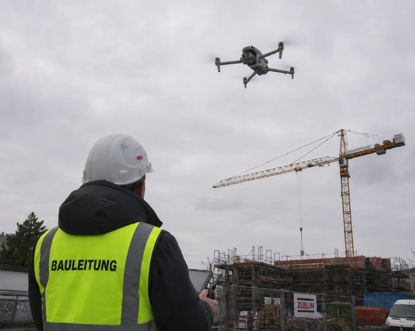 Bauleiter steuert DJI Matrice 4E Drohne zur Inspektion auf einer Baustelle mit Kran